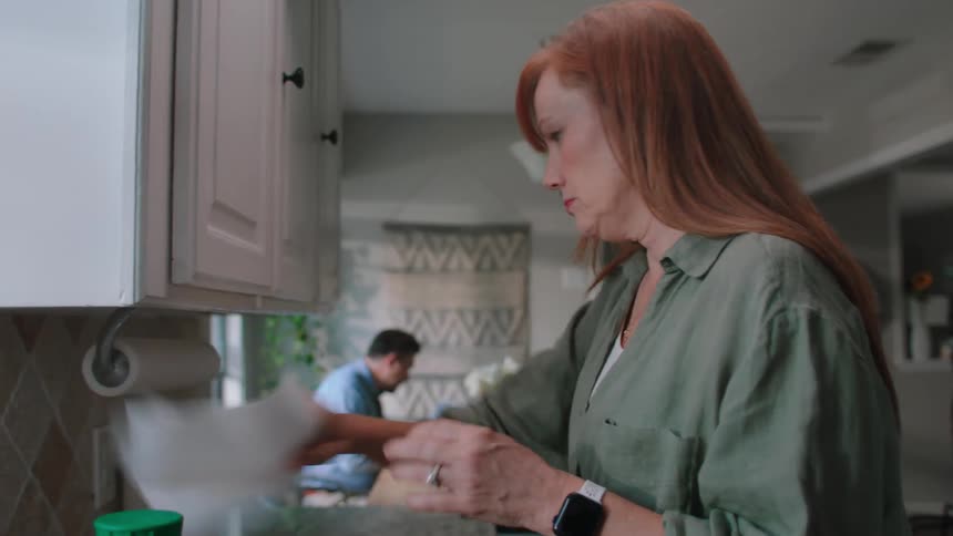 Woman in the kitchen preparing a bread with jam and taking a napkin and a glass cup from the cupboard