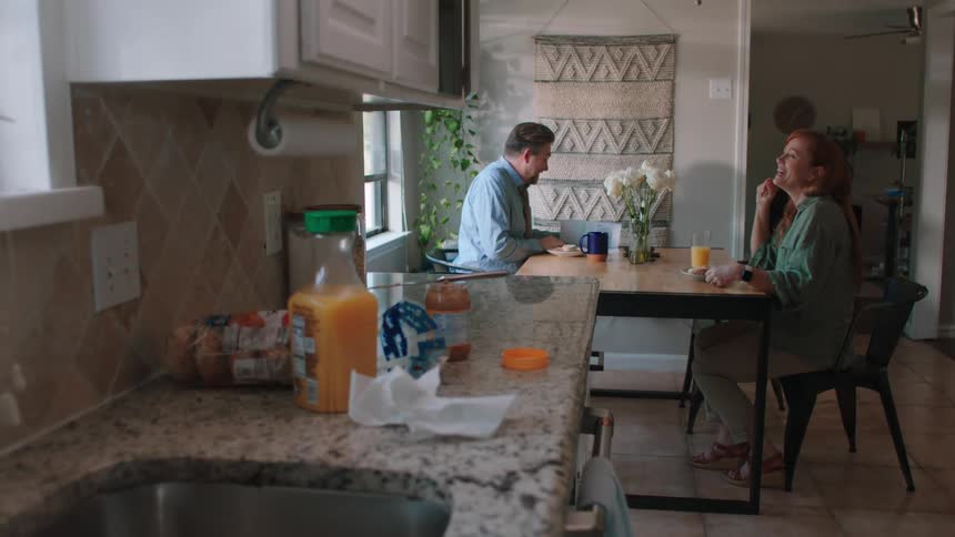 A couple sits at the kitchen table enjoying breakfast and engaged in conversation
