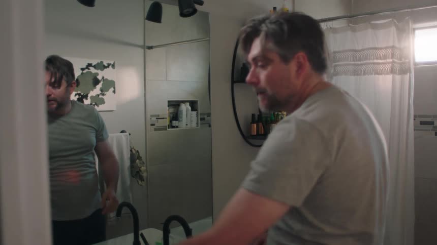 A tired man stands in front of the bathroom mirror at morning