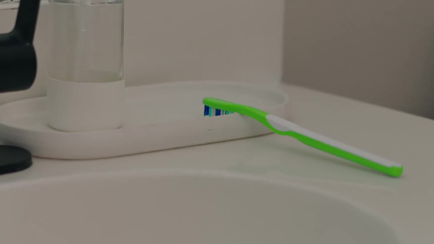 Hand picking up a green toothbrush from the sink