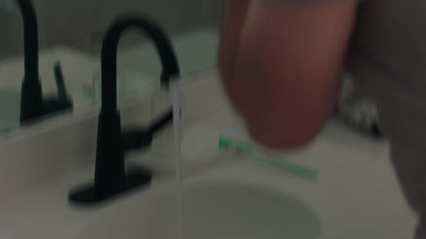 A nervous man rushes into the bathroom and begins washing his face at the sink