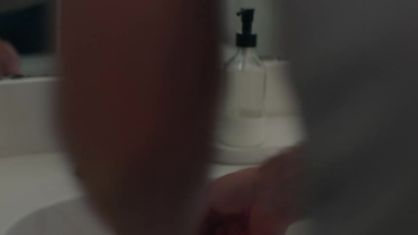 A man brushes his teeth in the bathroom sink