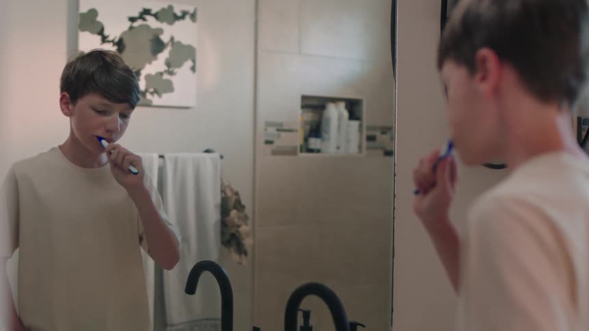Boy in front of the mirror in the bathroom brushing his teeth