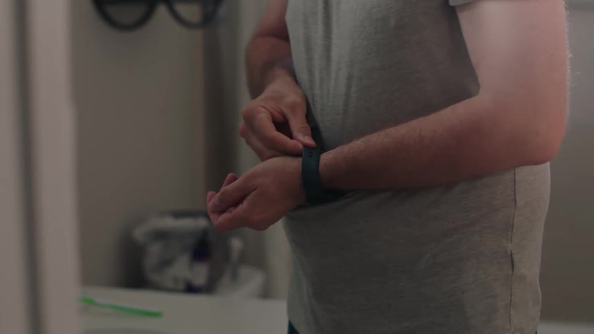 A man gets ready for the day in the bathroom putting on his smartwatch and ring
