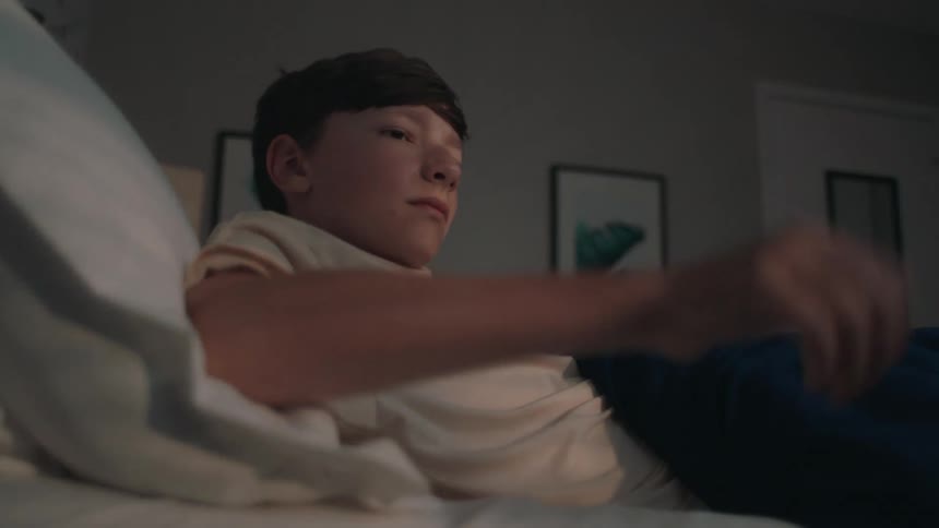 A young boy wakes up turns off his alarm clock and gets out of bed