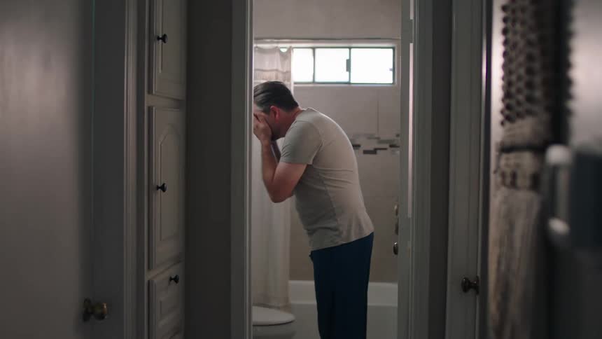A man walks to the bathroom and washes his face with water