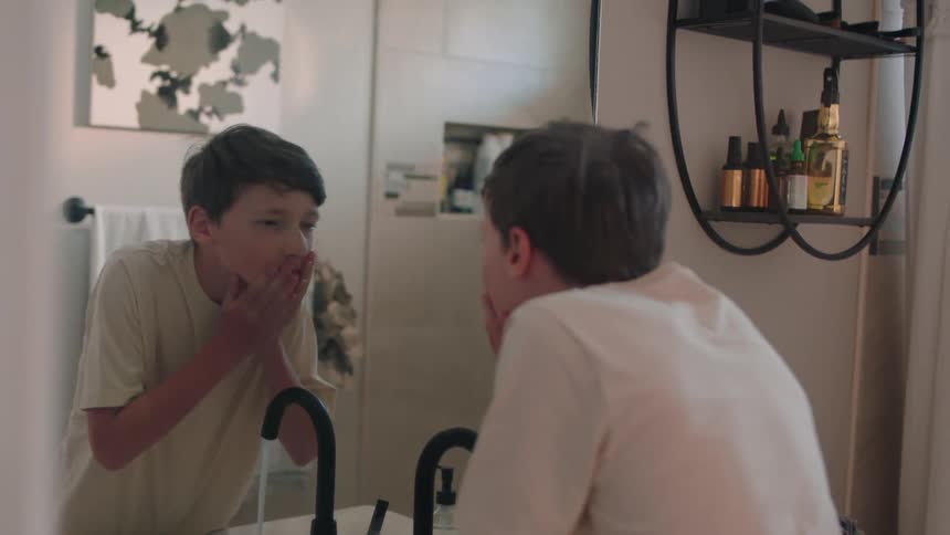 A teenage boy rinses his hands and face in the bathroom sink