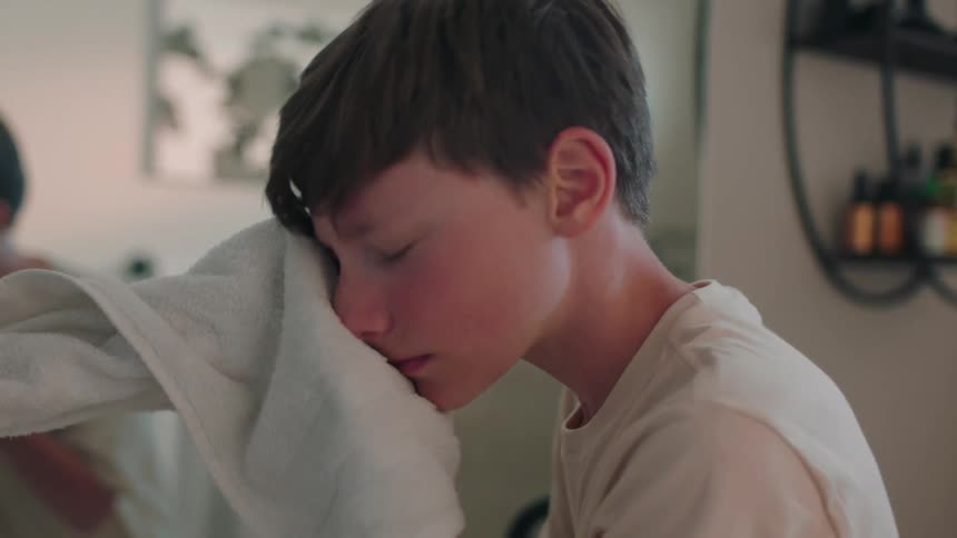 Portrait of a boy wiping his face with a towel in front of the mirror in the bathroom