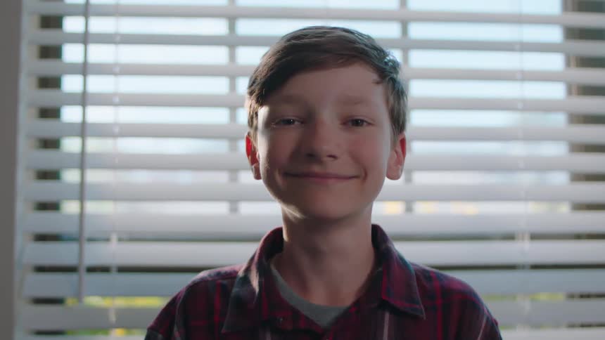 Close up of the face of a young boy standing in front of a window at home