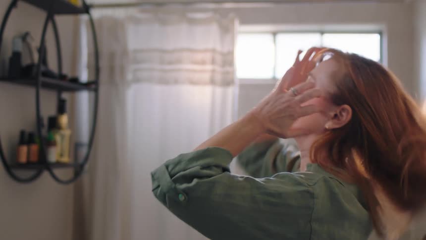 Woman putting on makeup and fixing her hair in front of the mirror in the bathroom