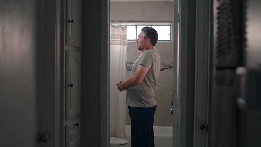 Man in bathroom washing his face and stretching his arms up