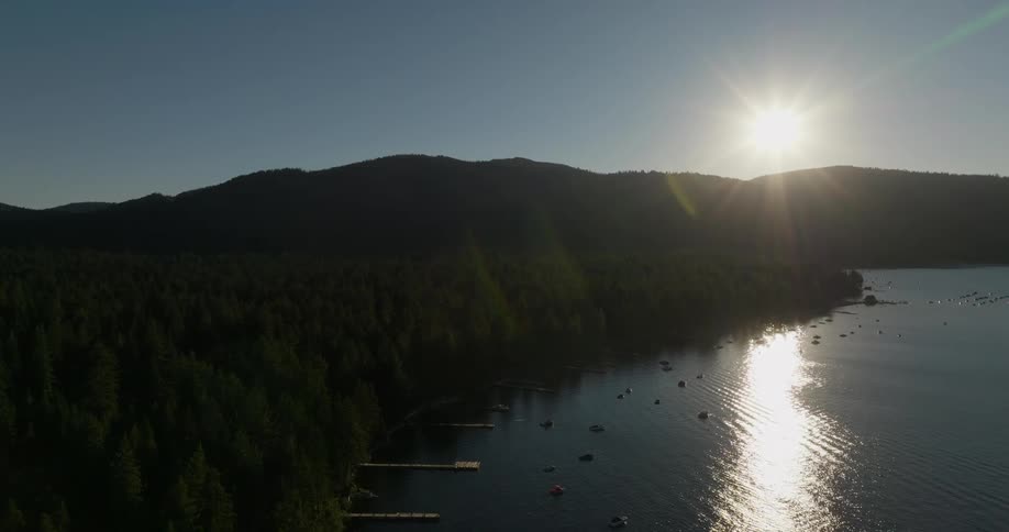 Aerial landscape with the sun on the horizon reflecting on a lake with a pier and the edge of mountains with vegetation