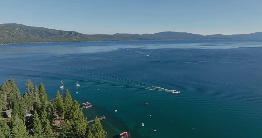 A serene lake surrounded by dense forest with a clear sky overhead a boat creates a wake on the water and smaller boats dot the scene