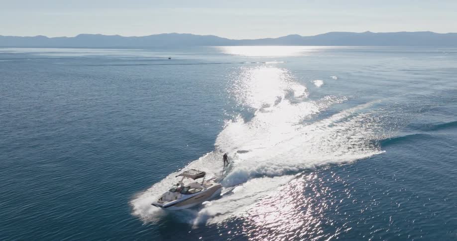 Person holding onto a rope on a moving yacht and surfing across a lake