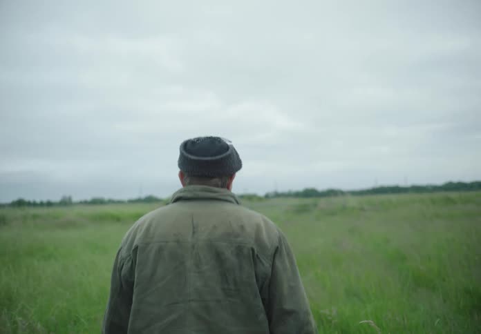 A man in a coat and cap walks across a large grassy field