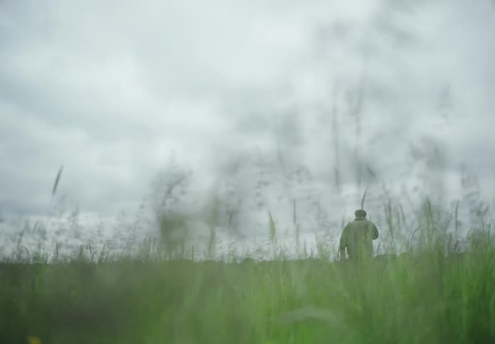 Man walking through a field with green grass and a cloudy day
