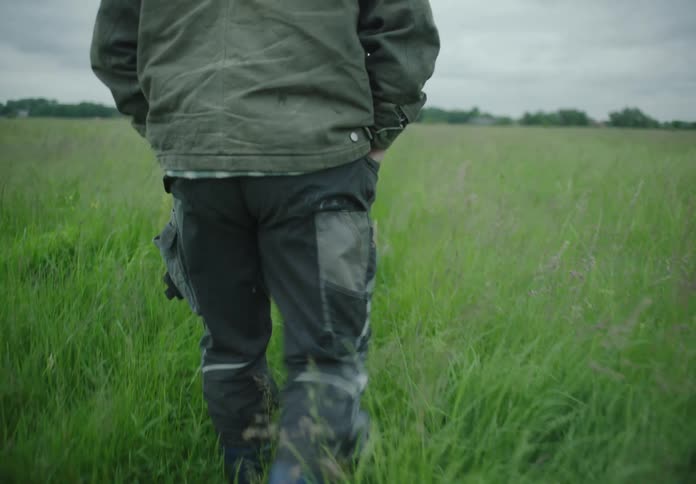 Legs of a person walking in a field with tall greenish grass