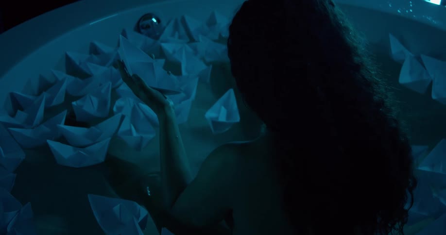 Curly haired woman sitting in bathtub with paper boats