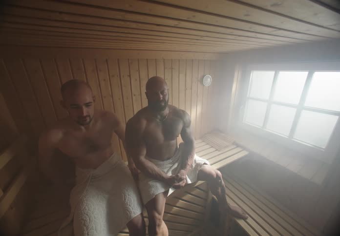 A man inside a wooden sauna room shifts uncomfortably and distances himself from the other person