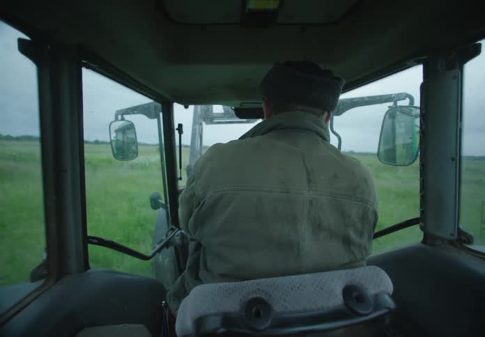 A farmer drives a tractor through a field of tall green grass