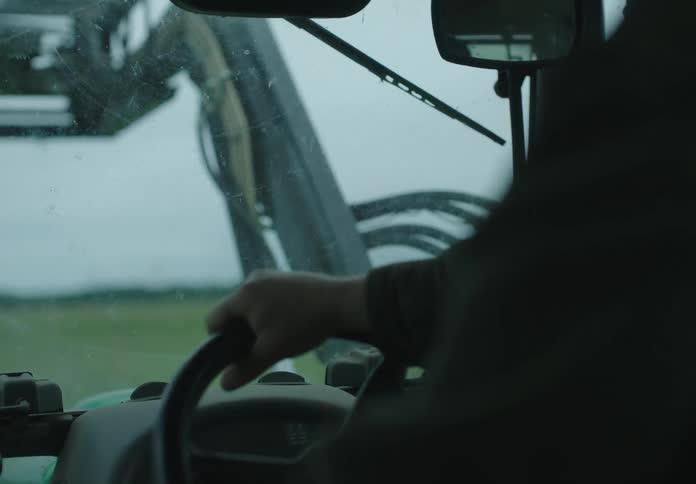 A man drives a tractor through a green field on a rainy morning