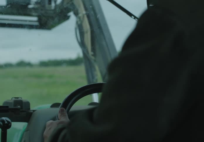 A person driving a tractor through a green field under an overcast sky