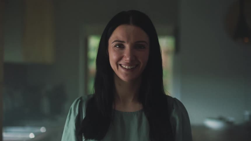 Woman stands smiling in dimly lit kitchen