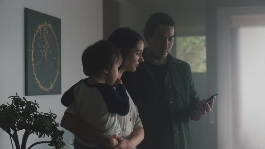 Parents holding a baby look at a cellphone in the living room at home