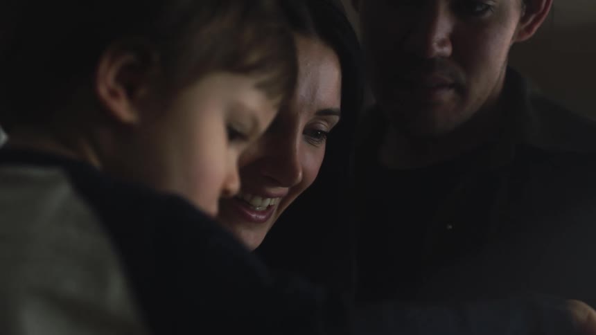 A close up of a father standing next to his son being held by his mother as they talk and smile