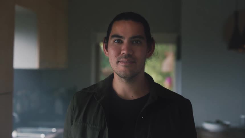 Man poses with slight smile while standing near kitchen
