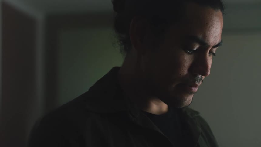Man with bun and dark shirt looks down in room