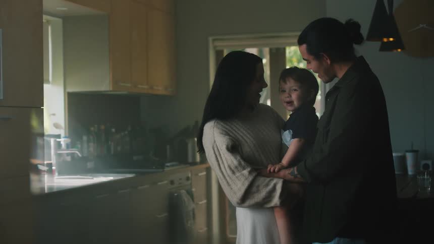 Father and mother hold toddler baby laughing in the kitchen