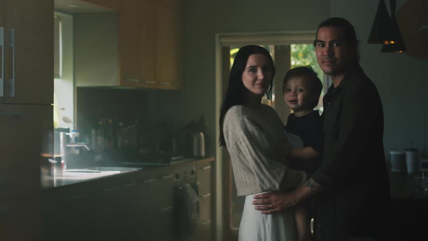 Father and mother stand close sheltering son between them as they pose in the kitchen