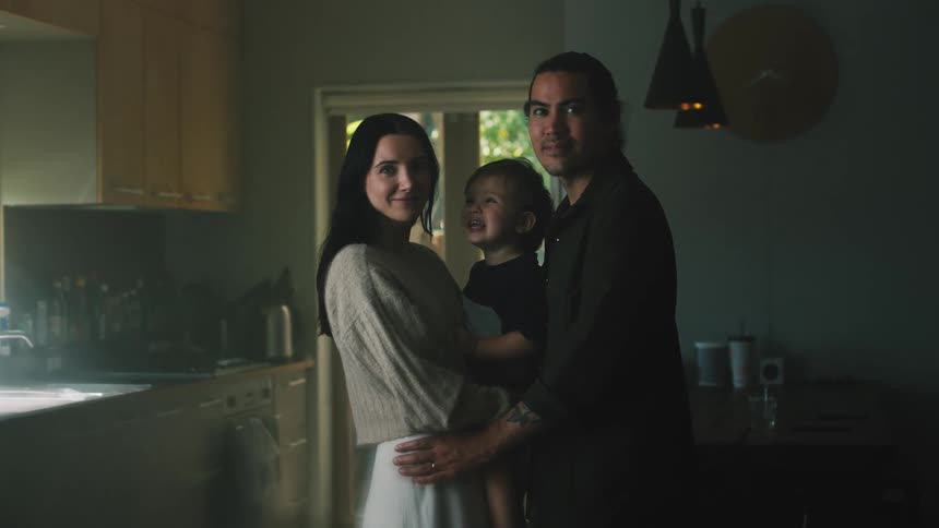 A man and a woman are standing in the kitchen with their young son