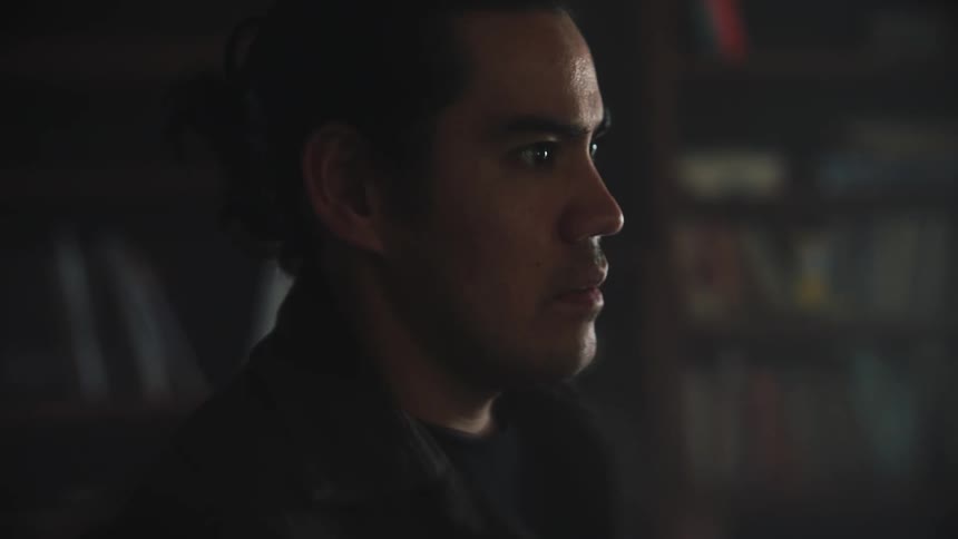 A worried looking man stands and breathes deeply as a woman carrying a baby back and forth walks behind him