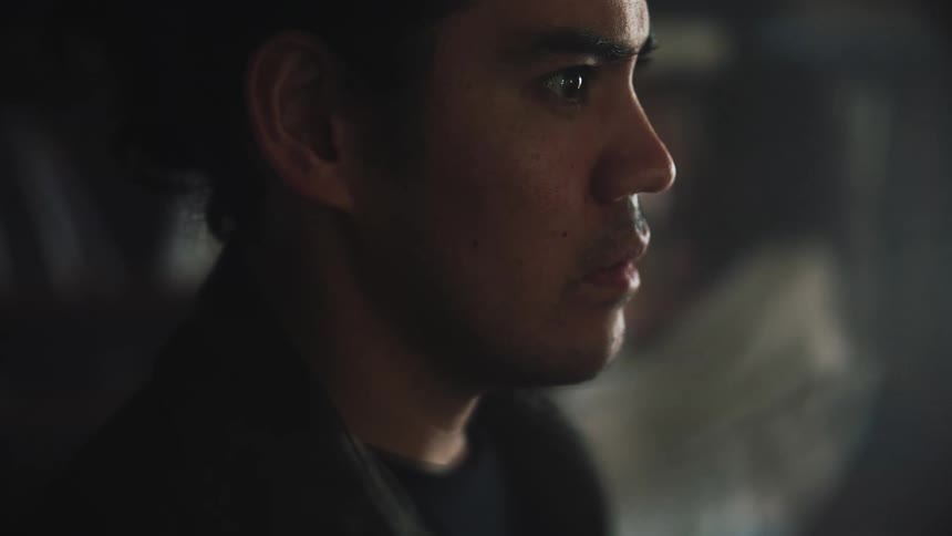 A sad looking man stands and looks in to the distance while a woman holding a baby paces back and forth behind him