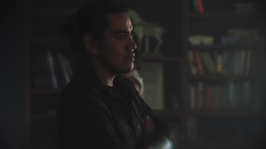 Father standing with his arms crossed as the mother and child walk back and forth near a bookshelf