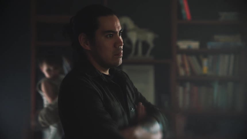 Man standing with arms crossed as mother and baby walk around next to a bookshelf
