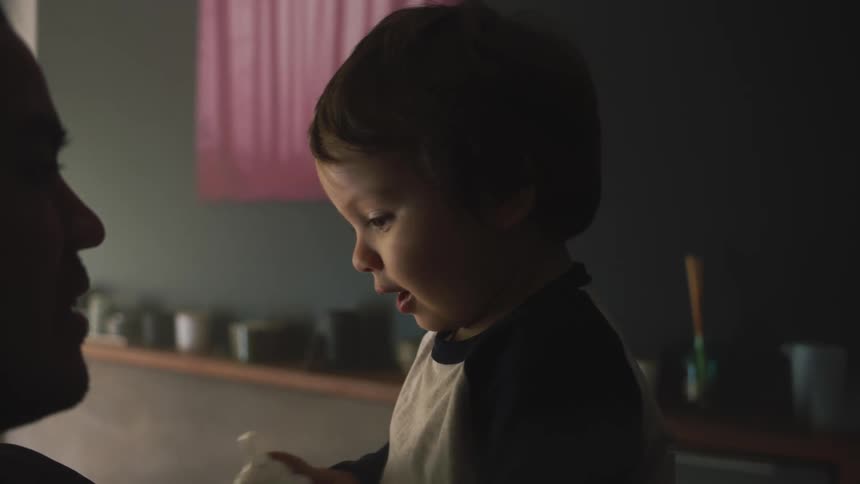 A father holding his toddler son while the boy holds a milk bottle and smiles