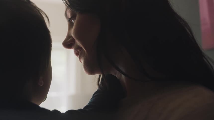 Mother with dark hair kisses toddler sons forehead laughing