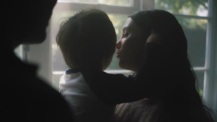 Close up of a mother talking and kissing his baby boy near a window at home