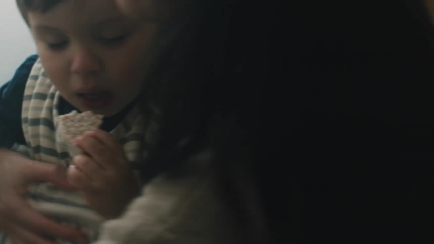 Woman with dark hair and sweater help toddler son eat and drink