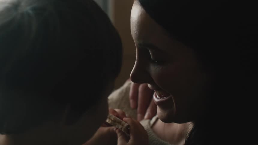 A woman kisses her son on the cheek while he eats a sandwich