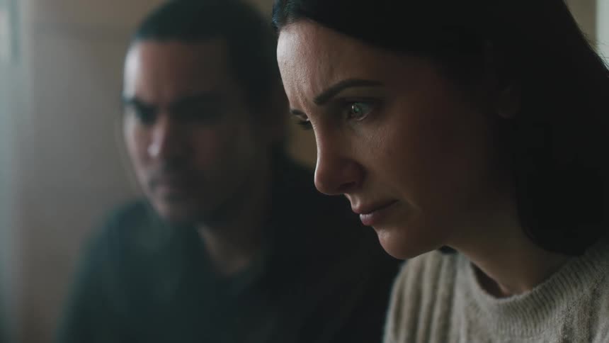 A man and woman sit near each other indoors while focusing their attention