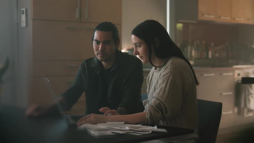 A man and woman use a laptop together at the kitchen table