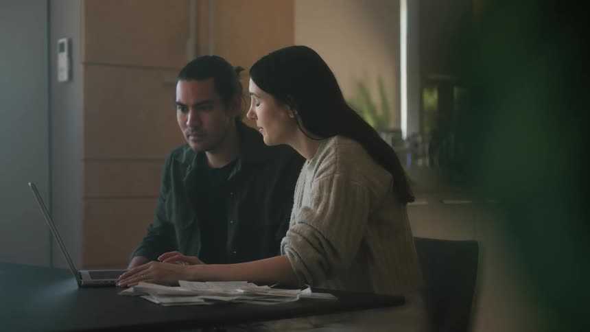 A man and woman sit at their kitchen table to pay bills online
