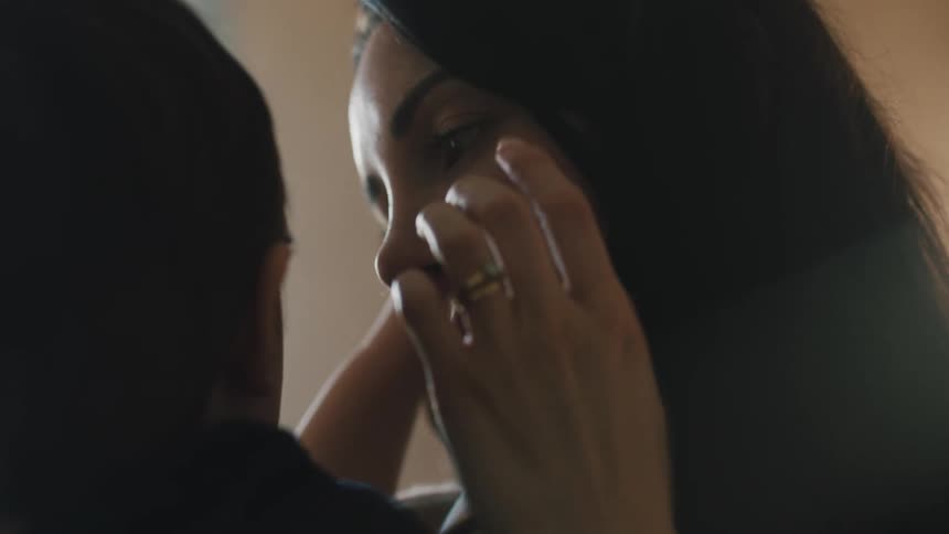 A woman is holding her young son and talking to him as she pushes his hair back with her hand