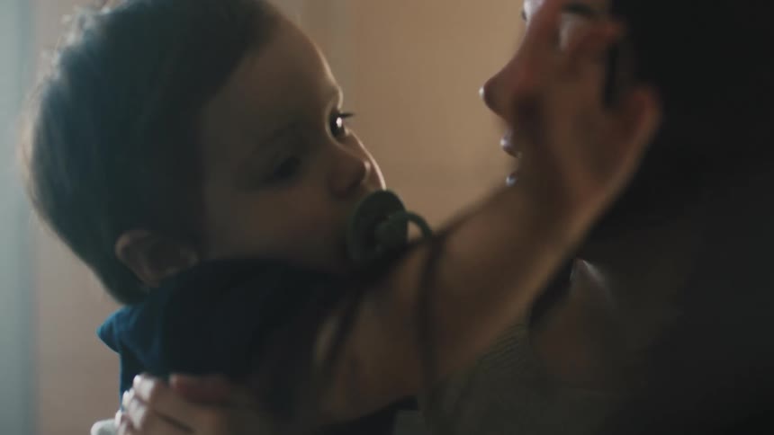 Mother holds and kisses her son as the child sucks on a pacifier and smiles