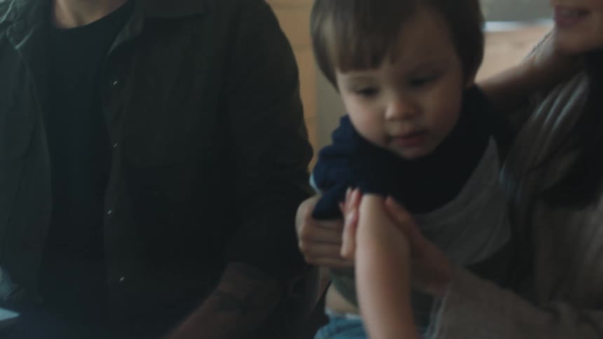Mother holding son sits next to the father smiling at the child