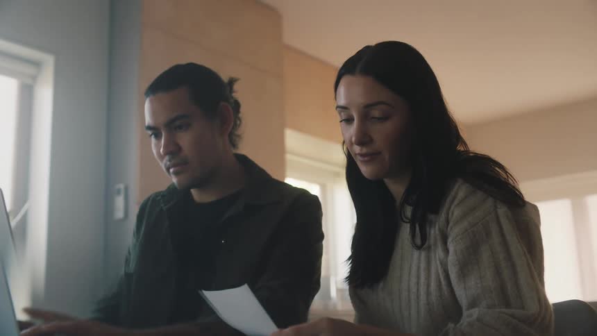 Woman with gray sweater reads man a note to type on laptop